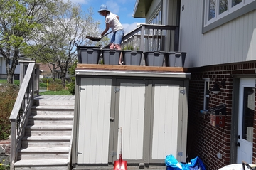 woman shoveling soil into container tubs top of a small shed
